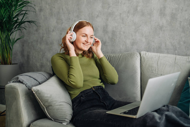 Навушники, ноутбук і жінка на домашньому дивані слухають музику або аудіо під час трансляції в Інтернеті. Спокійна жінка відпочиває на дивані, щоб слухати радіо чи пісню з підключенням до Інтернету та технологіями
 - Фото, зображення