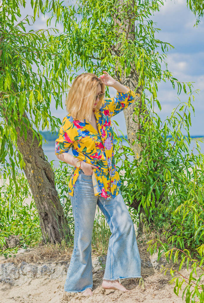 Nainen värikkäässä puuvillapaidassa ja soihdutetuissa farkuissa. Trendikkäitä vaatteita, lomakonsepti. Tyyli 70s - Valokuva, kuva