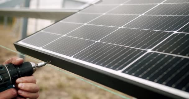 設置作業員はソーラーパネルを固定します。金属スタンドに太陽電池パネルを設置する技術者。金属プラットフォームシステムにソーラーパネルを設置する電動ドライバーで働く技術者. - 映像、動画