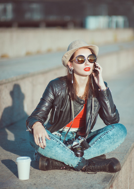 Хіпстерська дівчина в шкіряній куртці, капелюх з ретро камерою і мобільний
 - Фото, зображення