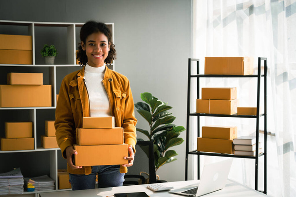 Afrikaans amerikaanse vrouw dragen pakket doos voor levering aan klant terwijl het werken in home office. - Foto, afbeelding