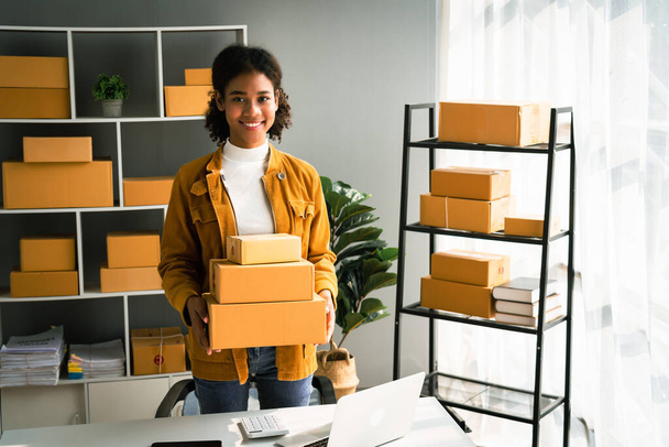 Afrikaans amerikaanse vrouw dragen pakket doos voor levering aan klant terwijl het werken in home office. - Foto, afbeelding