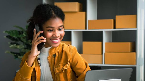 Femme afro-américaine parlant avec le client sur smartphone pour vérifier la commande et l'adresse en ligne. - Photo, image