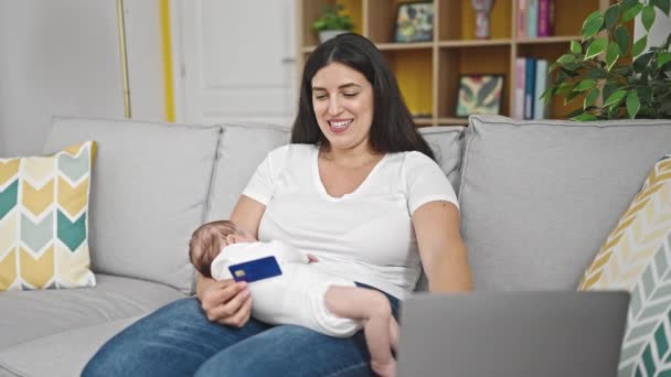 Мати і дочка, яка сидить на дивані, тримає дитину, робить покупки онлайн вдома - Кадри, відео
