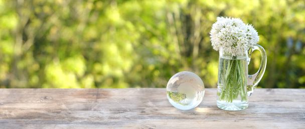 glass ball globe, bouquet of wild garlic flowers on old wooden table in garden, beautiful blurred natural landscape in background with green foliage, Ecology concept, energy of nature for renewable - Foto, afbeelding