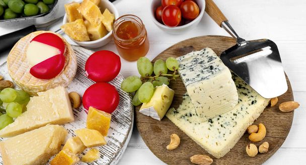 Different kinds of cheese served with green olives, tomato and grape for gourmet nutrition. Organic parmesan and brie with honey delicatessen - Fotoğraf, Görsel