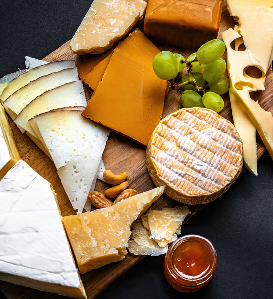 さまざまな種類のチーズは、グルメ栄養のためのブドウと蜂蜜を提供しています。有機パルメザンとハードチーズセットのデリカテッセン - 写真・画像