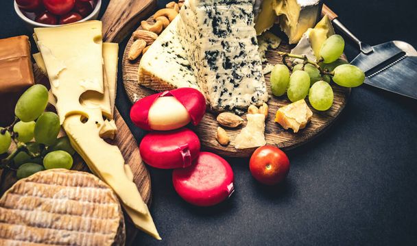Different kinds of cheese served with grape and tomato for gourmet nutrition. Organic brie and camembert set with nuts delicatessen on black table - Foto, immagini