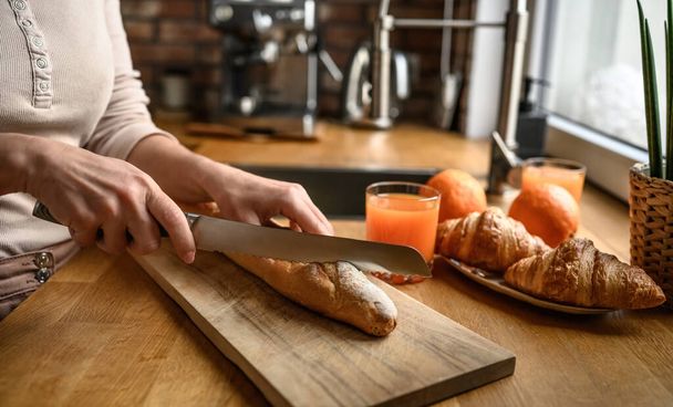 Girl hand cut french baguette with knife at kitchen. Tasty rustic fresh bread from France for breakfast meal - Foto, afbeelding