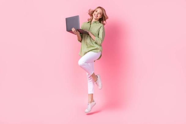 Full length photo of pretty adorable woman dressed green shirt jumping high working modern device isolated pink color background. - Zdjęcie, obraz