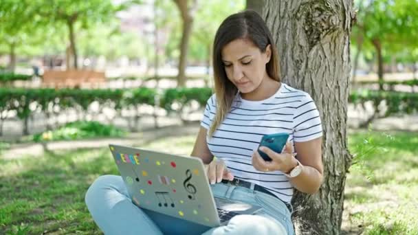 Lähi-idän nainen käyttää kannettavaa tietokonetta ja älypuhelinta puistossa - Materiaali, video