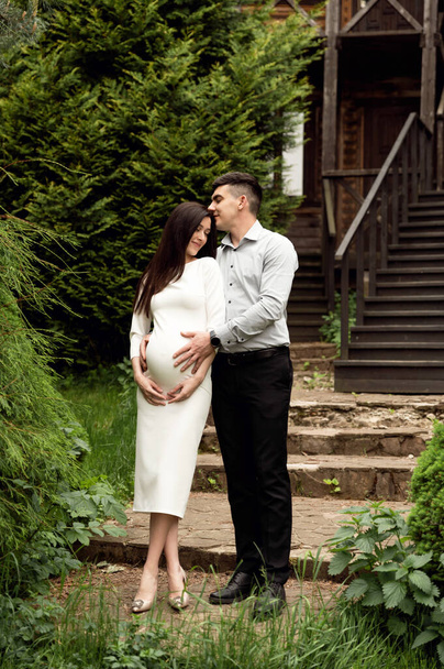 a married couple gently hugs against the background of a wooden ecological house. wife is pregnant. man gently hugging a pregnant woman - Zdjęcie, obraz