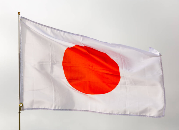 Large flag of Japan fixed on metal stick waving against background of cloudy sky during daytime - Zdjęcie, obraz