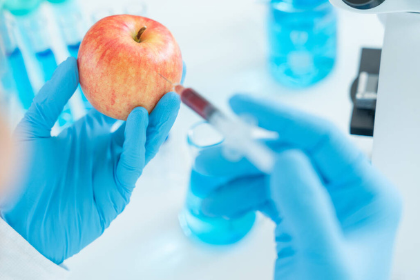 A tudósok ellenőrzik a kémiai élelmiszer-maradványokat a laboratóriumban. Ellenőrző szakértők ellenőrzik a gyümölcs minőségét, tudósok befecskendezik a vegyi anyagokat az almába kísérletezés céljából, veszélyek, tiltott anyag, szennyeződés - Fotó, kép