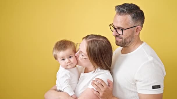 Anne, baba ve bebeğin ailesi izole edilmiş sarı arka planda öpüşüyor. - Video, Çekim