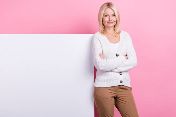Portrait of pleasant person blond hair dressed white sweater standing near empty space arms folded isolated on pink color background. - Photo, image