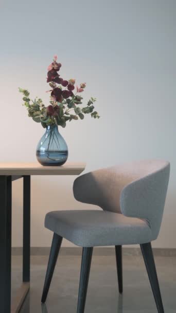 Un video verticale per i social media. Una mano muove un moderno vaso di vetro blu su un tavolo con una sedia grigia. Filmati FullHD di alta qualità - Filmati, video