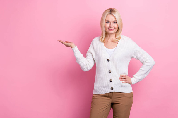 Portrait of good mood friendly retired person wear white sweater palm demonstrate product empty space isolated on pink color background. - Foto, Imagen