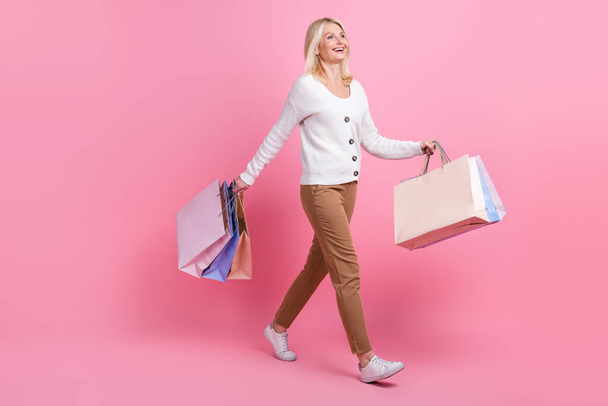 Full body profile portrait of positive pretty lady hold bags walking isolated on pink color background. - Фото, зображення