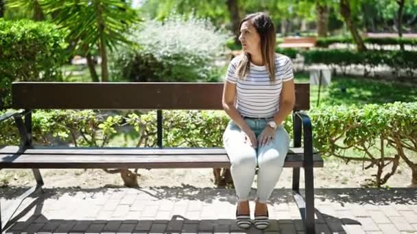 中東の女性が周りを見回し,公園で一人でベンチに座っている時計を見ている - 映像、動画