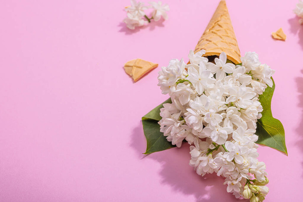 White lilac flowers in waffle ice cream cones on pink background. Flat lay, hard light, dark shadow, traditional spring concept, copy space - Photo, Image