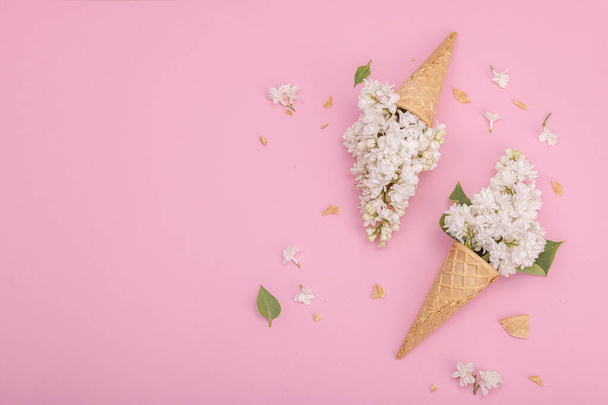 Белые сиреневые цветы в вафельных рожках мороженого на розовом фоне. Плоская кладка, традиционная концепция пружин, вид сверху - Фото, изображение