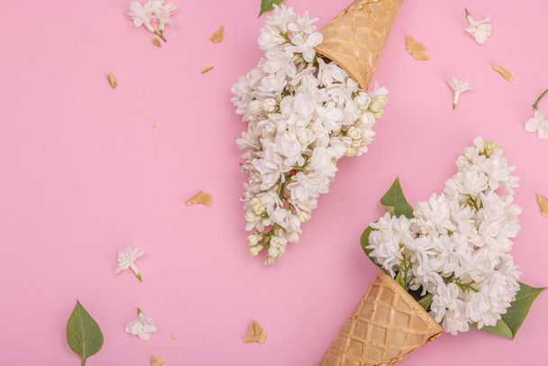 Valkoinen lila kukkia vohveli jäätelöä käpyjä vaaleanpunainen tausta. Tasainen lay, perinteinen kevät konsepti, ylhäältä - Valokuva, kuva