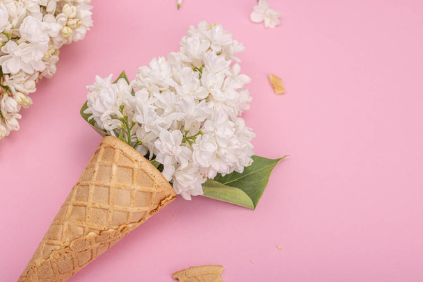 Flores de color lila blanco en conos de helado de gofre sobre fondo rosa. Colocación plana, concepto de primavera tradicional, espacio de copia - Foto, Imagen