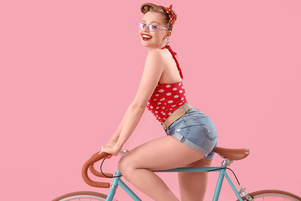 Young pin-up woman with bicycle on pink background - Фото, зображення