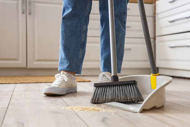 Домогосподарка прибирає підлогу з мітлою і пиломатеріалом на кухні, крупним планом
 - Фото, зображення