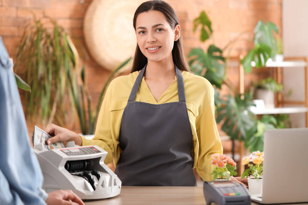 Female cashier using cash counting machine in flower shop - Photo, Image