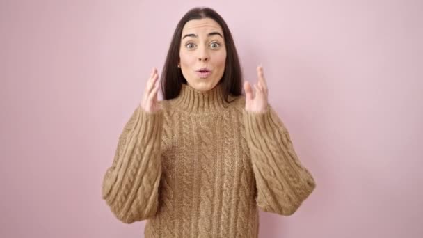 Junge schöne hispanische Frau steht mit überraschendem Gesichtsausdruck vor isoliertem rosa Hintergrund - Filmmaterial, Video