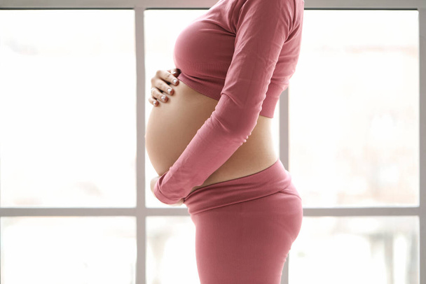 Sporty pregnant woman near window at home, closeup - Photo, Image