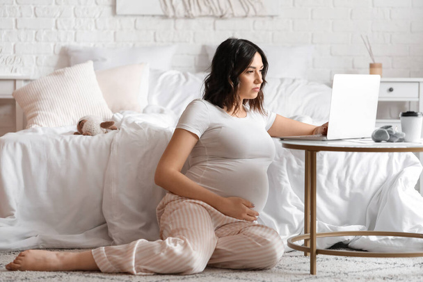 Νεαρή έγκυος γυναίκα που εργάζεται με φορητό υπολογιστή στο υπνοδωμάτιο - Φωτογραφία, εικόνα