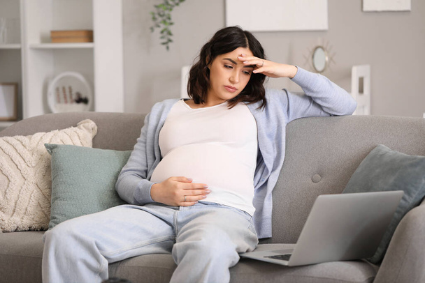 Moe jonge zwangere vrouw werken met laptop thuis - Foto, afbeelding