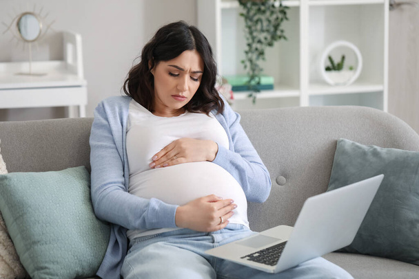 Уставшая молодая беременная женщина работает дома с ноутбуком - Фото, изображение