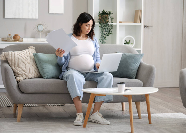 Young pregnant woman working with documents and laptop at home - Фото, зображення