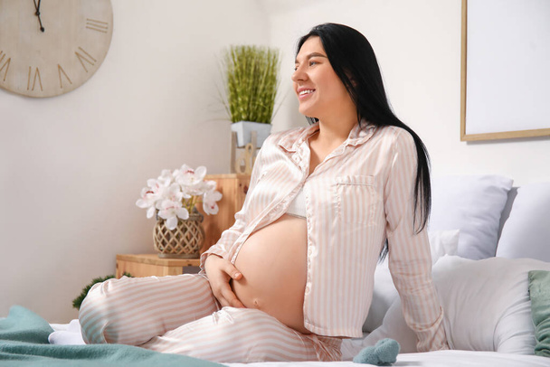 Giovane donna incinta seduta in camera da letto
 - Foto, immagini