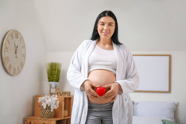 Young pregnant woman with heart in bedroom - Valokuva, kuva