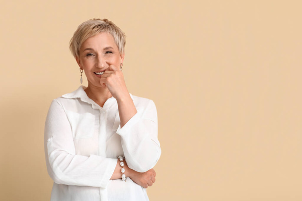 Mature blonde woman in white shirt on beige background - Foto, afbeelding