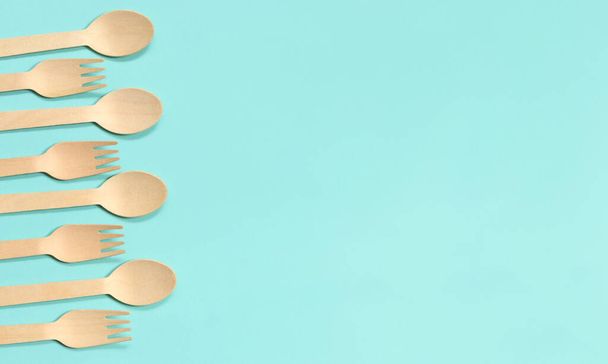 Wooden disposable forks and spoons on a blue background, top view. Eco friendly disposable kitchen utensils, copy space. Flat lay - Valokuva, kuva