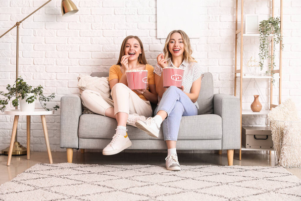 Junge Schwestern essen Popcorn auf Sofa zu Hause - Foto, Bild