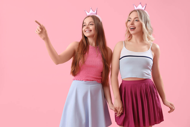 Young sisters in crowns holding hands on pink background - Photo, Image