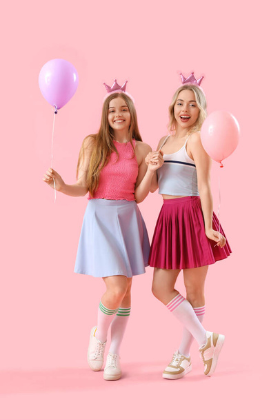 Hermanas jóvenes en coronas con globos sobre fondo rosa - Foto, imagen