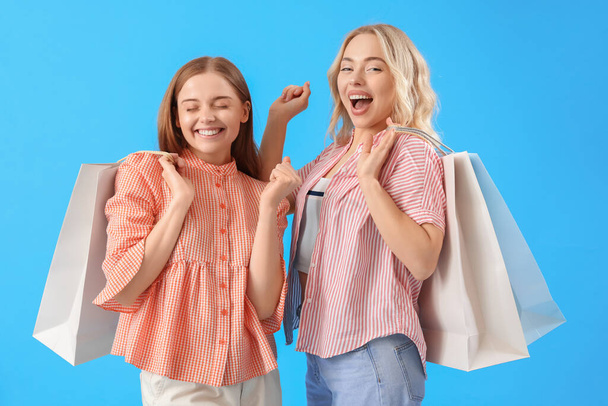 Νεαρές αδελφές με τσάντες για ψώνια σε μπλε φόντο - Φωτογραφία, εικόνα