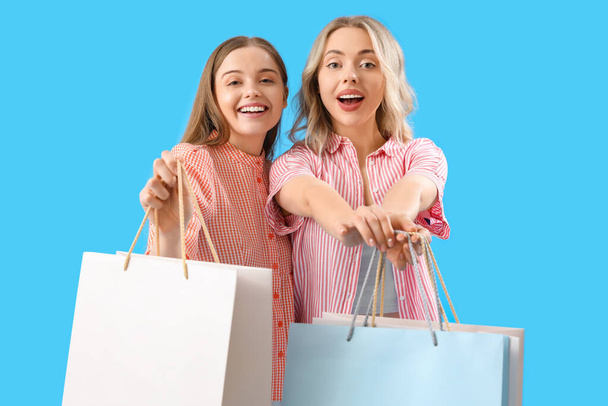 Hermanas jóvenes con bolsas de compras sobre fondo azul - Foto, Imagen