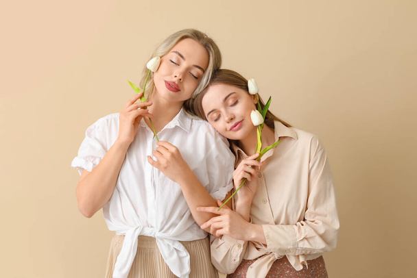 Young sisters with tulips on beige background - Photo, Image