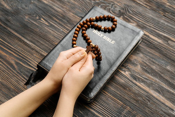 Mani femminili con perline di preghiera e Sacra Bibbia su sfondo di legno - Foto, immagini