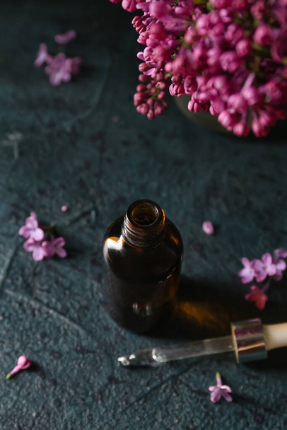 Bottiglia di olio cosmetico con bellissimi fiori lilla su tavolo scuro - Foto, immagini