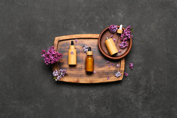 Composition with bottles of lilac essential oil and flowers on dark background - Фото, зображення